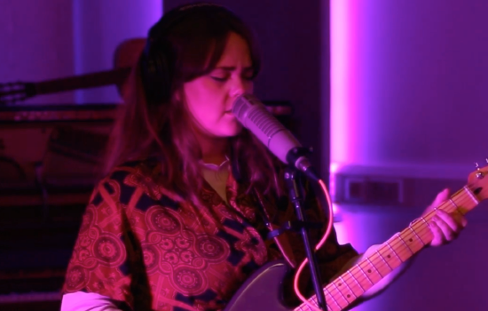 A photograph of a woman playing guitar and singing into a microphone.