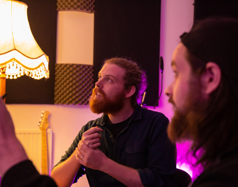 A photograph of James Bennett, COO of RouteNote, and Ed Pipkin, Head of Artist Services. James has a beard and long ginger hair tied back in a bun, and Ed has a beard and long brown hair worn loose. Ed is also wearing a backwards snapback.