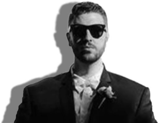 A black and white photograph of artist Stevo Jacobs. He has short light hair and a beard, and is wearing dark sunglasses with a dark suit jacket, a light-coloured button shirt, and a light bowtie.